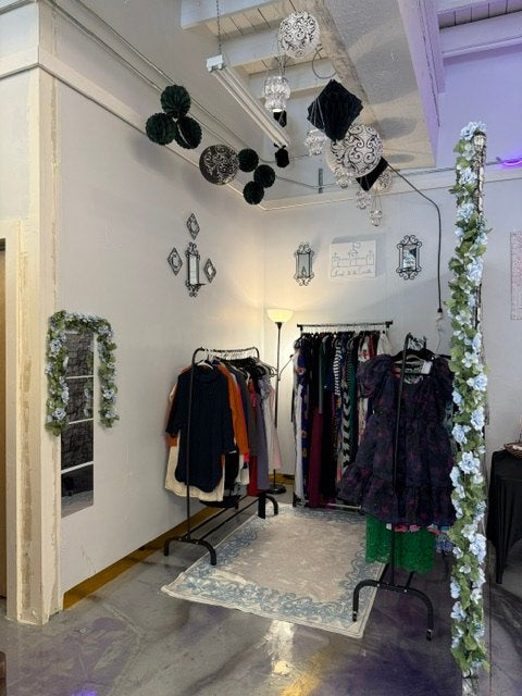 A curated vendor booth with clothing racks, floral decor, and hanging ornaments