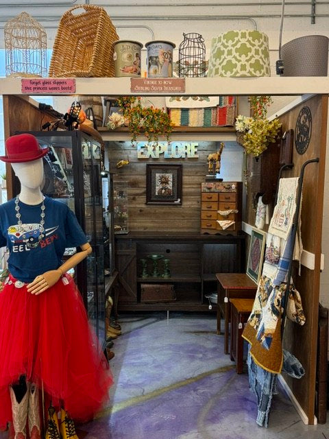 A vendor booth with a mannequin, display cases, baskets, and collectible home decor