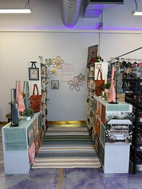 A colorful vendor booth with tote bags, shelves, and handmade gift items