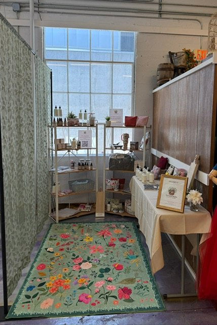 A bright vendor booth with shelves, small goods, and a floral rug